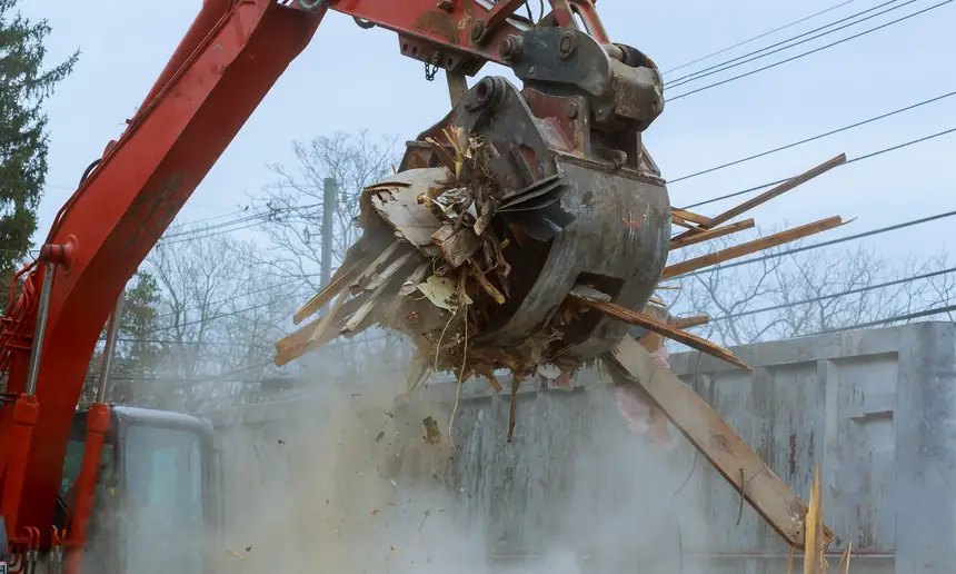 Excavator grapple dropping demolition timber into a roll-off container