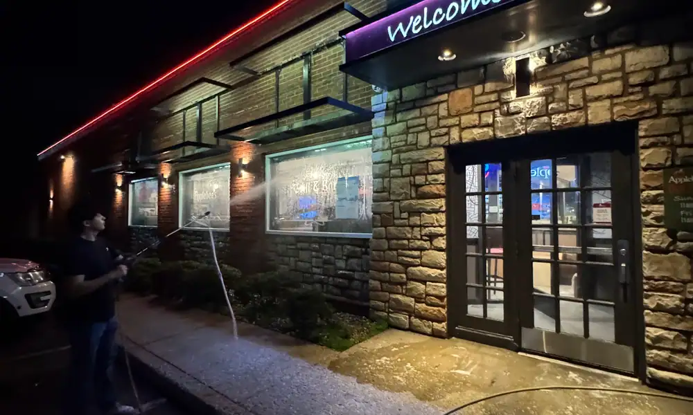 Crew pressure washing a storefront walkway at night