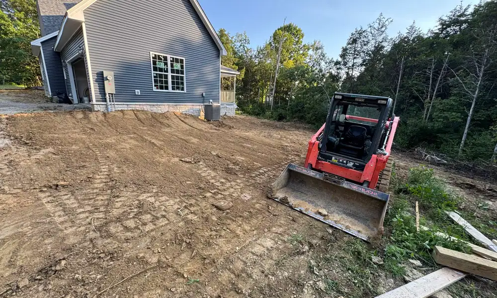 Skid steer grading bare ground beside a new house