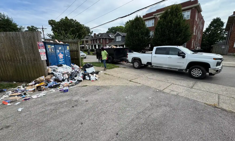 Pile of trash beside a fence, with trucks and trailers ready to haul it