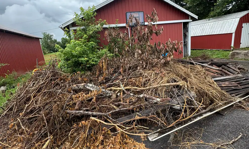 Brush and debris piled beside a red barn